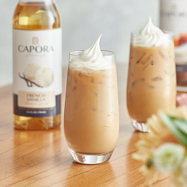 A glass of brown liquid with a Capora French Vanilla flavoring syrup bottle.