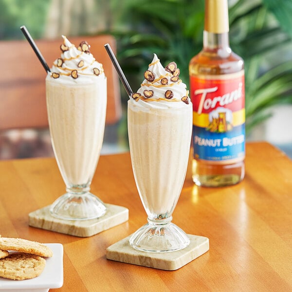 Two glasses of milkshakes with whipped cream and chocolate chips on a table.