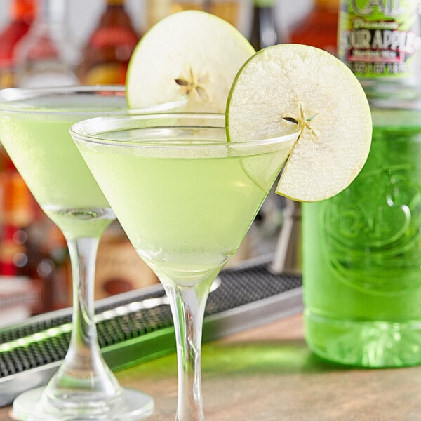 A glass of green liquid with a slice of apple on the rim.