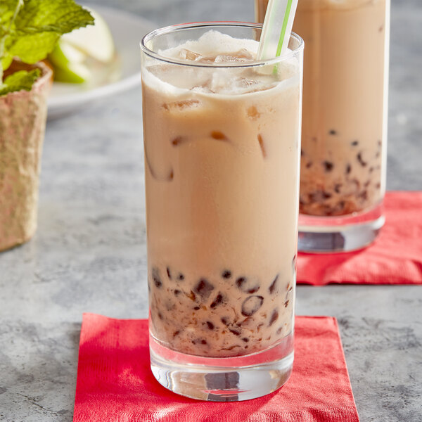 A glass of milk tea with brown liquid and a straw.