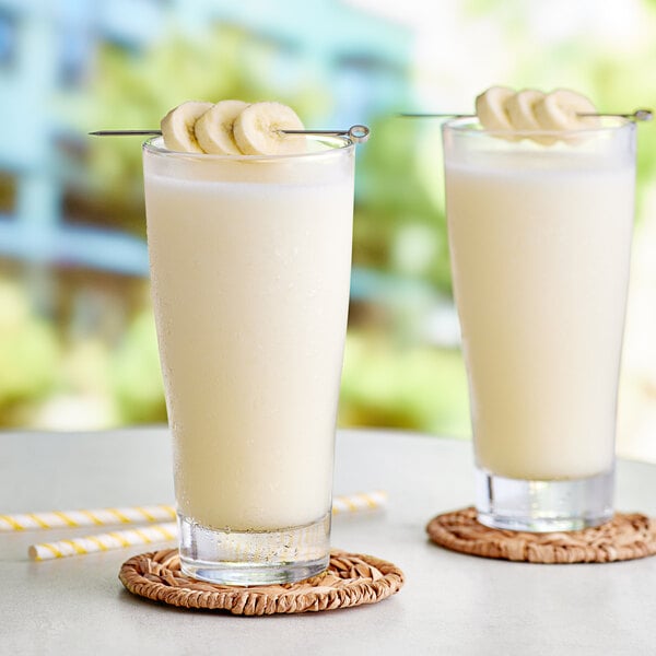 Two glasses of banana smoothies with straws on a white background.