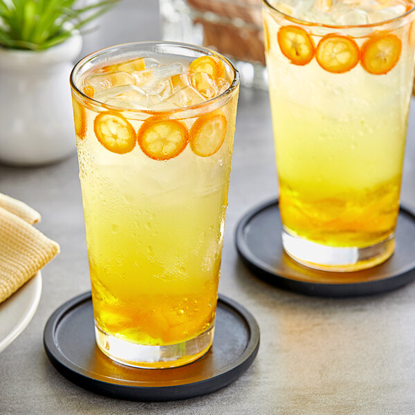 A pair of glasses with a drink made with Fanale Kumquat Concentrated Syrup and ice, garnished with orange slices.