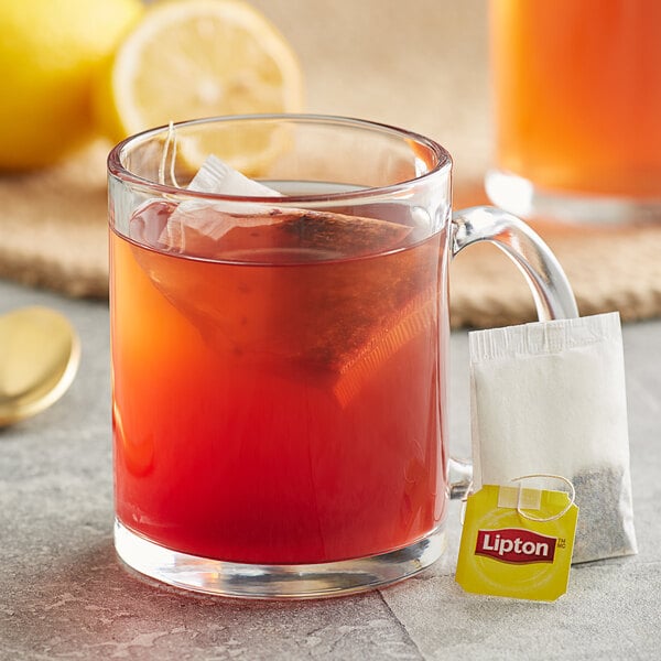 A glass mug with a Lipton Lemon Herbal Tea bag in it.