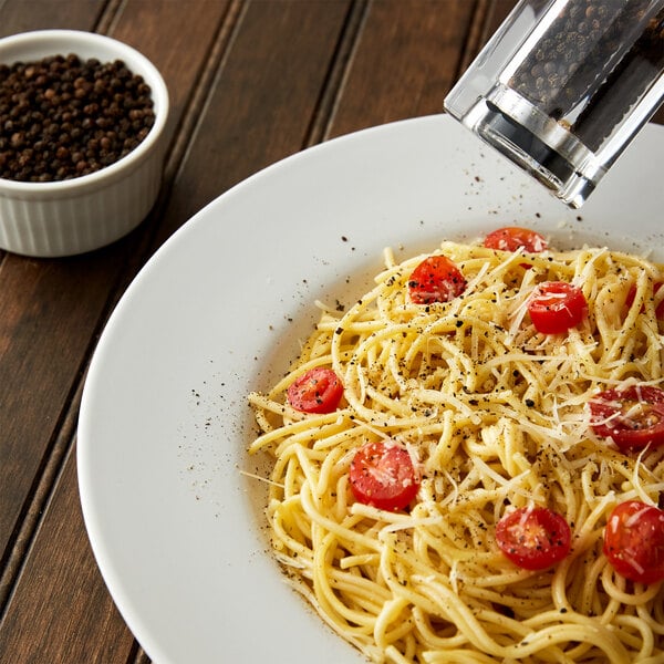 A bowl of spaghetti with tomatoes and black peppercorns on top.