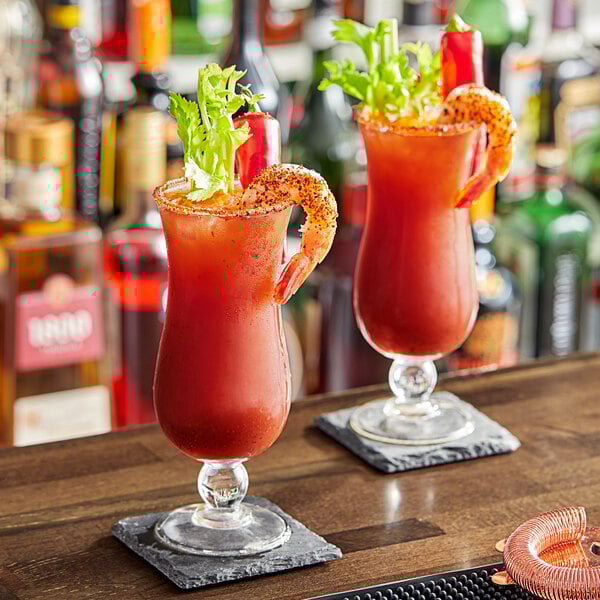 Two glasses of Zing Zang Blazing Bloody Mary with shrimp on top on a bar.