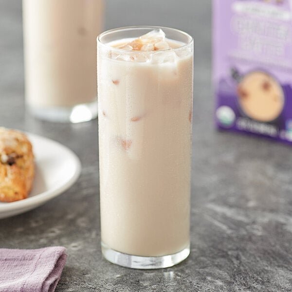 A glass of Oregon Chai Organic Slightly Sweet Chai Tea Latte over ice with a plate of cookies.