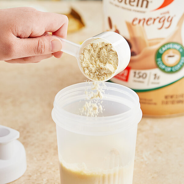 A hand holding a scoop of Premier Protein Cafe Latte powder over a container.