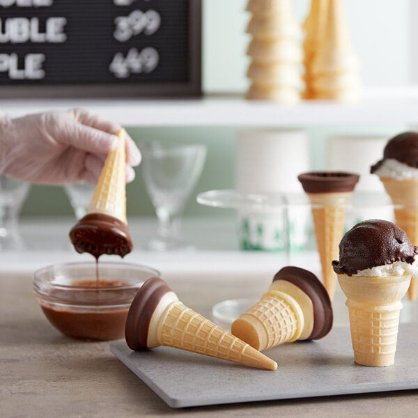 A person pouring Phillips chocolate sauce into an ice cream cone.