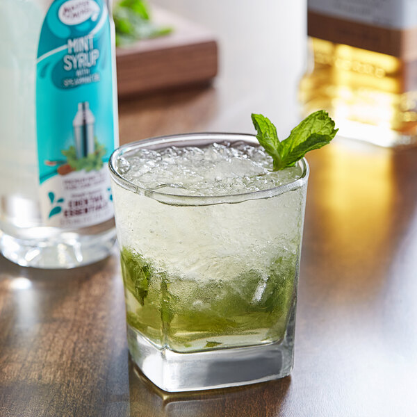 A glass with a drink and a green leaf on top next to a bottle of Master of Mixes Premium Mint Syrup.