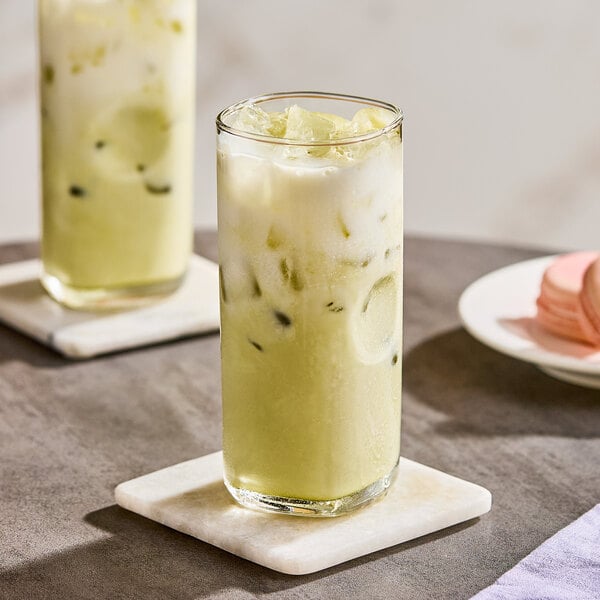 A tall glass of iced matcha green tea latte with a creamy layer on top, served on a marble coaster.