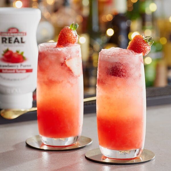 Two glasses of red drinks with strawberries on top on a table.