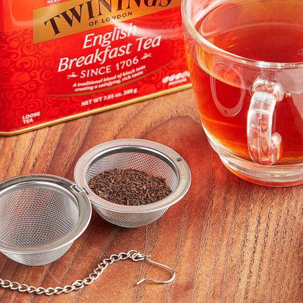 A Twinings tea strainer with loose tea leaves in a cup of tea.