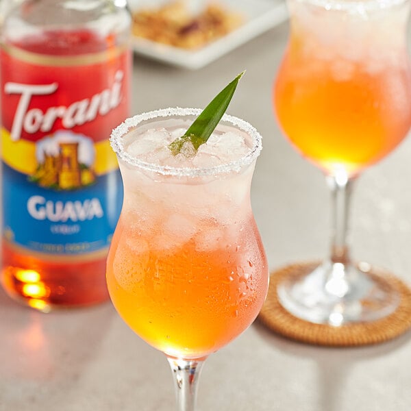 A close-up of two glasses of orange guava drinks with leaves on top.