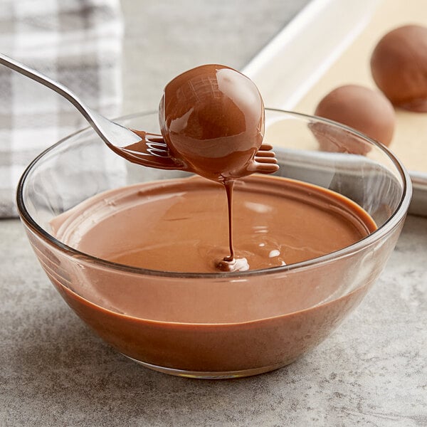 A spoon dipping a chocolate ball into liquid chocolate in a bowl.