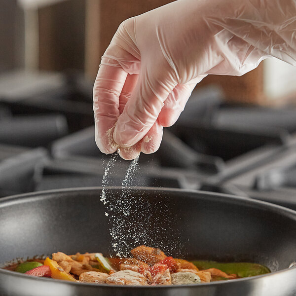 A person in gloves sprinkling Regal Organic Onion Powder onto food in a pan.