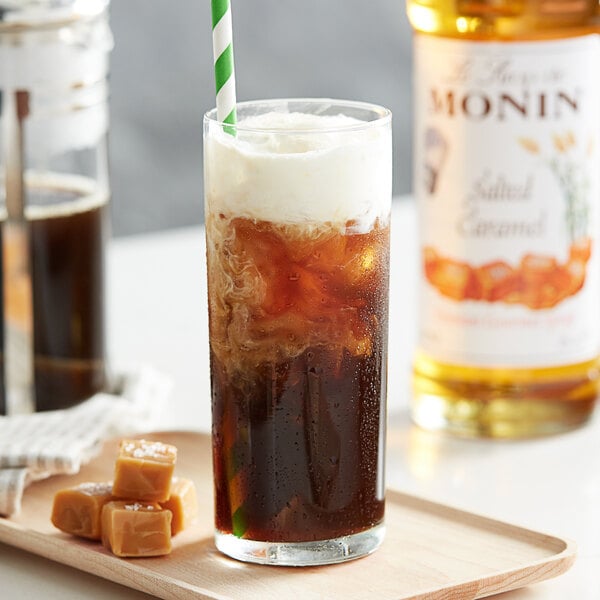 A glass of brown liquid with ice and Monin Salted Caramel Flavoring with a brown straw.