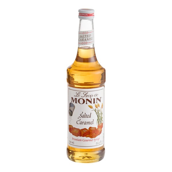 A clear glass bottle filled with a golden liquid, labeled as salted caramel syrup with images of caramel pieces and decorative text on the front.