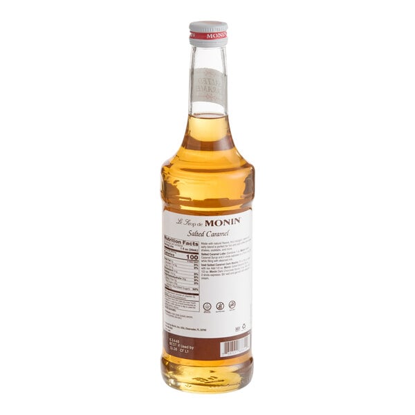 A clear glass bottle filled with a golden liquid, featuring a white label with text and a silver cap.