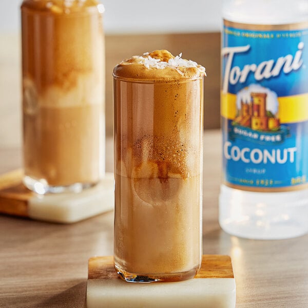 A glass of brown liquid with Torani Sugar-Free Coconut Flavoring Syrup and coconut flakes.