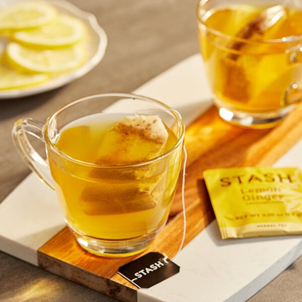 A glass mug of Stash Lemon Ginger herbal tea with a tea bag in it and lemons on the table.