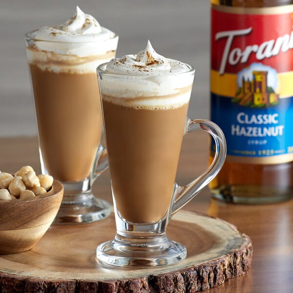 Two glasses of coffee with Torani Classic Hazelnut syrup, whipped cream, and nuts.