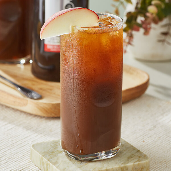 A glass of SHOTT Black Tea and Peach concentrate with ice and an apple slice.