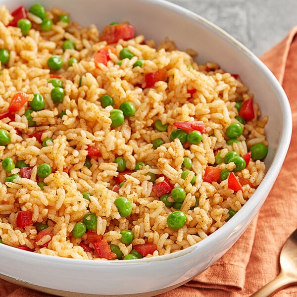 A bowl of rice with peas, tomatoes, and annatto on a cloth with a spoon.