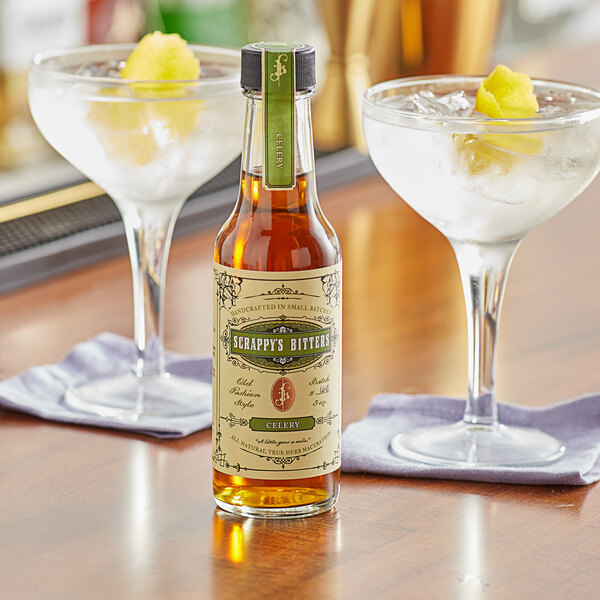 A bottle of Scrappy's Celery Bitters next to two glasses of liquid.