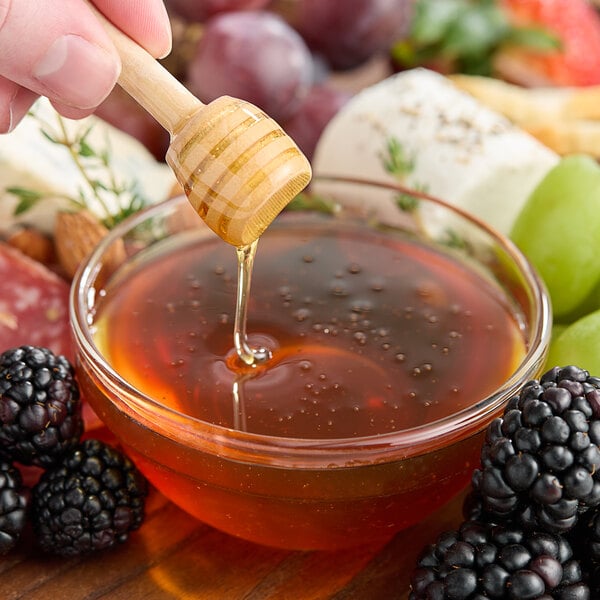 A wooden honey dipper drizzling Hometown Provisions Orange Blossom Honey into a bowl of liquid.