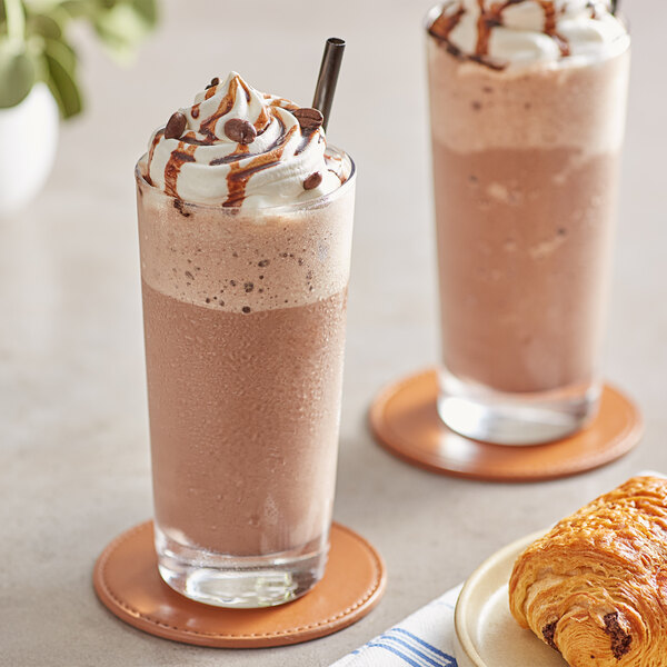 Two glasses of Frozen Bean Mocha Latte blended ice coffee with whipped cream and croissants on a table.