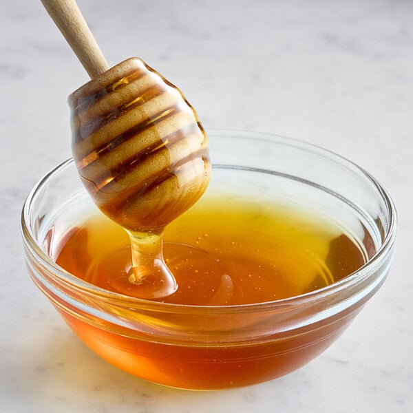 A honey dipper dripping Hometown Provisions Wildflower Honey into a bowl.