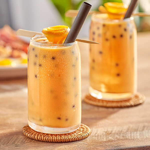 Two glasses of Fanale orange drink with straws and a fruit slice on a table.