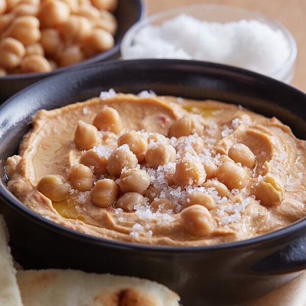 A bowl of hummus with chickpeas and a sprinkle of salt on top.