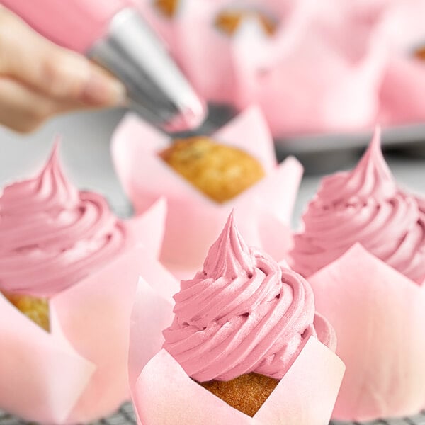 A hand using a pastry brush to frost a cupcake with Chefmaster rose pink food coloring.