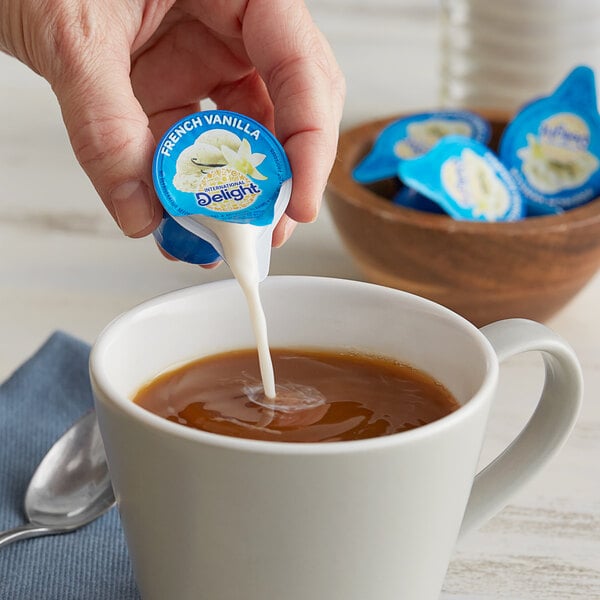 A person pouring International Delight French Vanilla creamer into a cup of coffee.