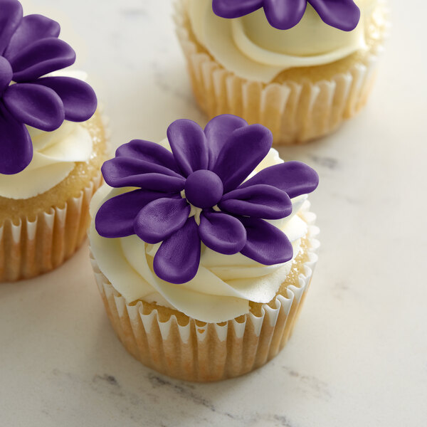 Three Satin Ice ChocoPan purple cupcakes with purple flowers on top.