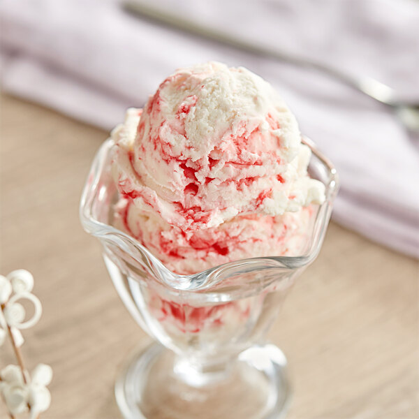 A glass cup with a scoop of strawberry ice cream and red and white sprinkles.