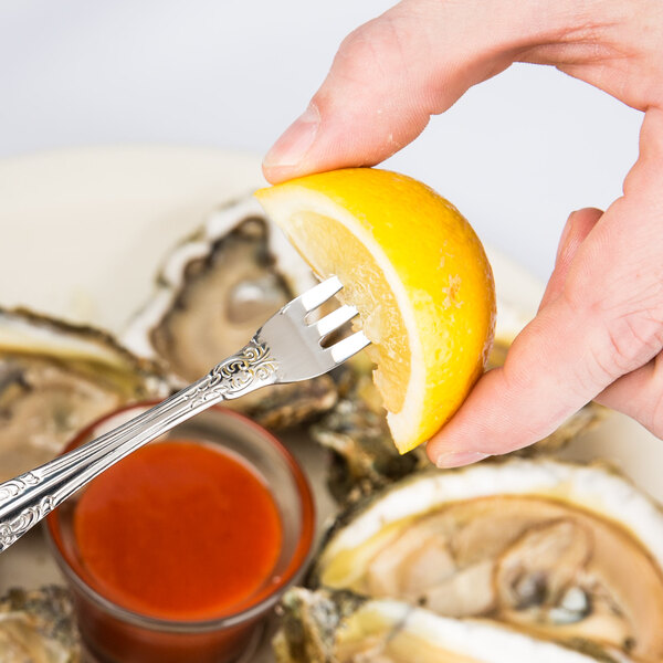 Oneida Rosewood stainless steel fork holding a lemon wedge over a bowl of sauce.