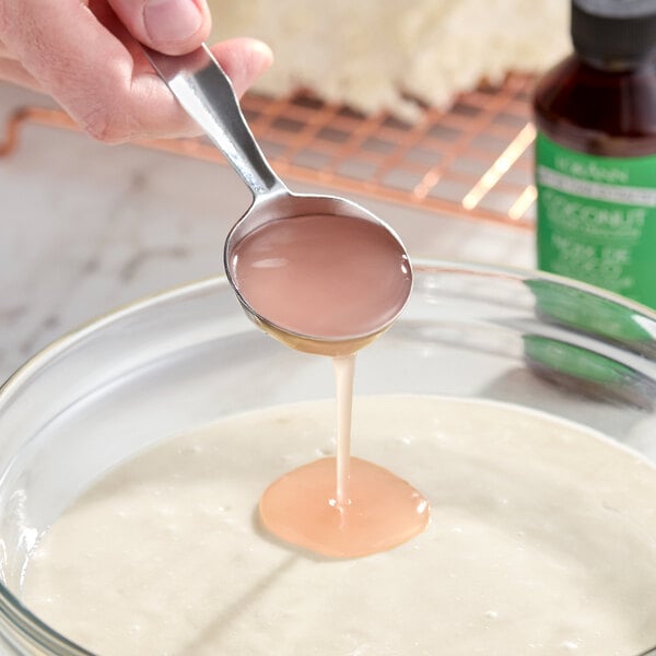 A spoonful of coconut bakery emulsion being poured into a bowl of batter.