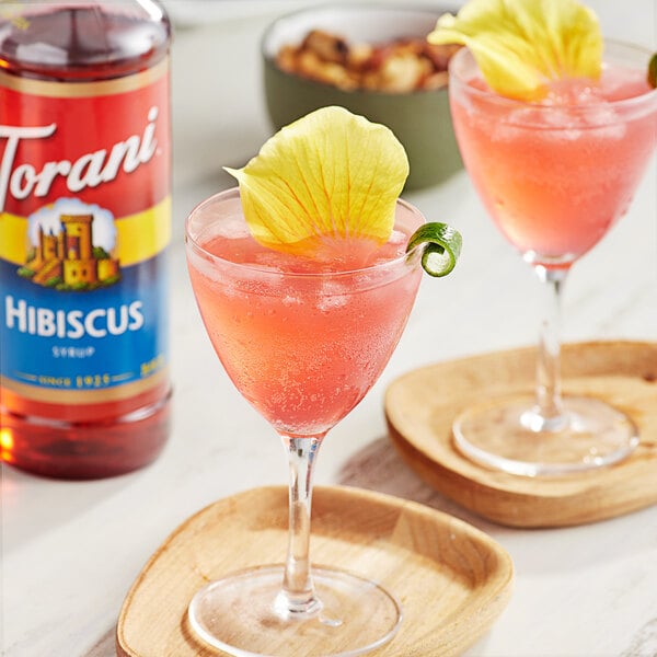 Two glasses of pink hibiscus drinks with flowers on top.