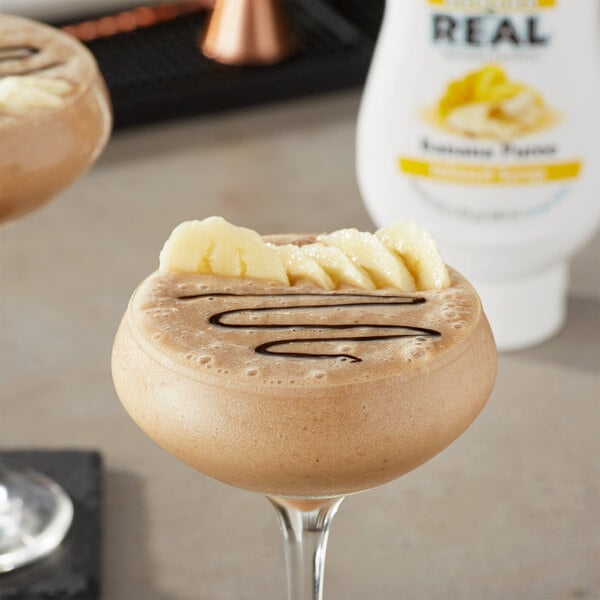 A brown drink with chocolate and banana slices on top in a glass.