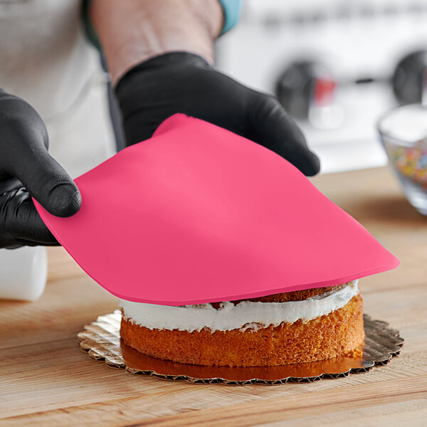 A person wearing black gloves and holding a pink cloth over a cake with Satin Ice Pink Vanilla Rolled Fondant.