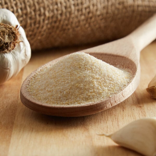 A wooden spoon filled with Regal garlic salt next to garlic cloves and powder.