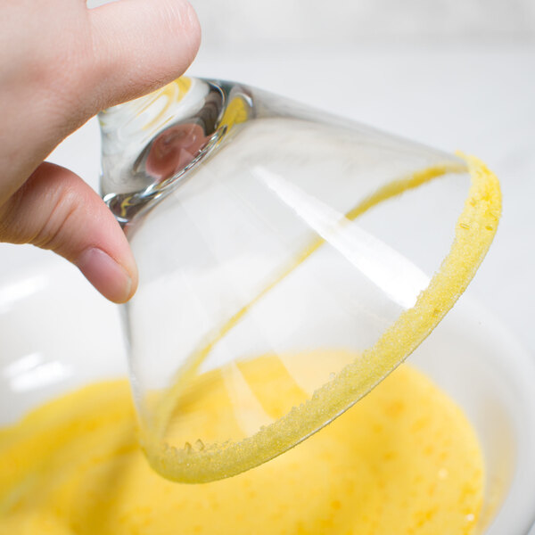 A hand rimming a glass with Rokz lemon cocktail sugar with yellow liquid.