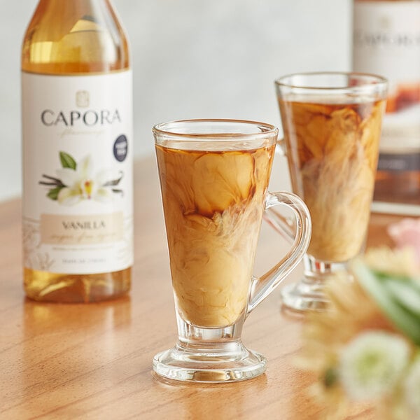 A bottle of Capora sugar free vanilla flavoring syrup next to a glass of brown liquid.