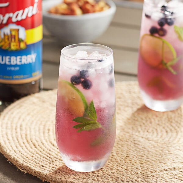 A glass of pink fruit drink with a straw and ice flavored with Torani Blueberry Syrup.