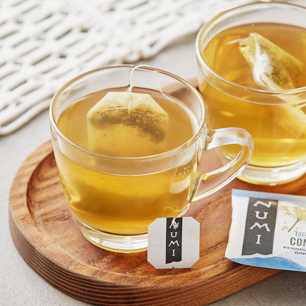 A pair of glass mugs of Numi Organic Congest Away tea with tea bags in them.