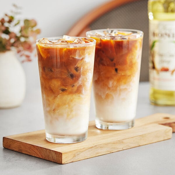 Two glasses of Monin pure cane syrup iced coffee on a wooden board.