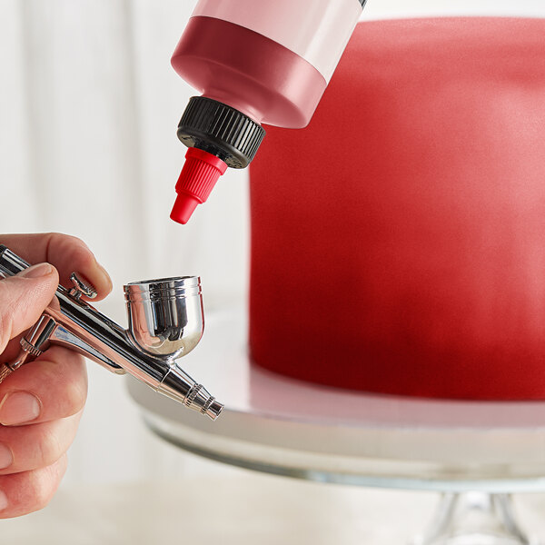 A person using a Chefmaster metallic red airbrush to spray red liquid onto a silver object.