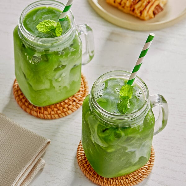 Two glass jars of green Matcha lattes with straws on a table.